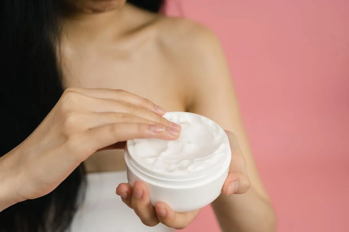A hand holding an open jar of face cream